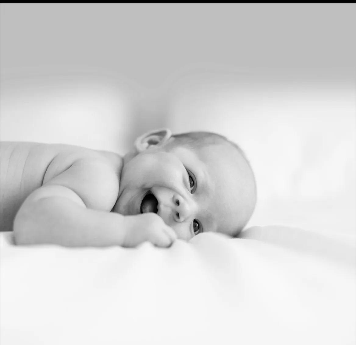 Black-and-white photograph of a smiling baby lying on a bed