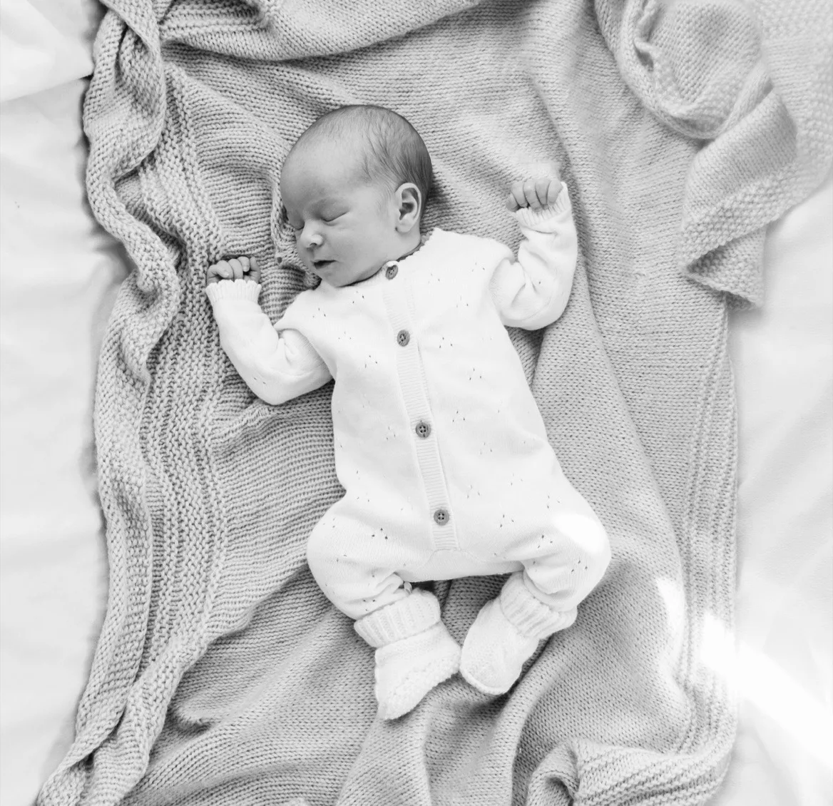 Black-and-white photograph of a newborn sleeping on a knitted blanket